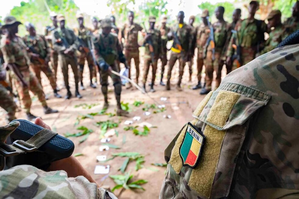 A platoon lieutenant from Benin engages in a training exercise to combat civil threats, discussing tasks using a sand table diagram.